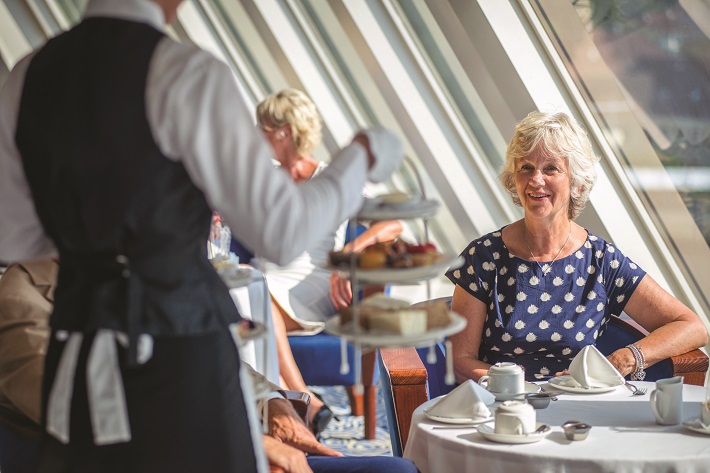 Lady being served afternoon tea on-board Fred. Olsen Balmoral