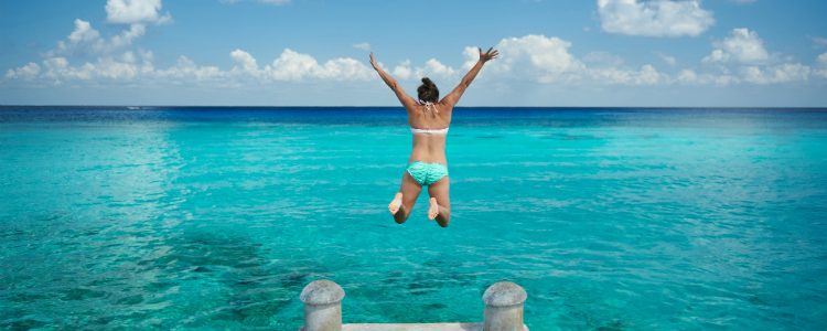 A woman jumping into the bright blue Caribbean sea during a solo cruise